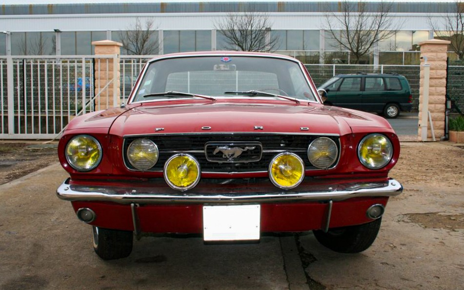 Vue de face de la Mustang GT 1966 version Export, arborant la configuration unique à six phares avec des optiques Marchal Equilux Ford et Marchal 610.