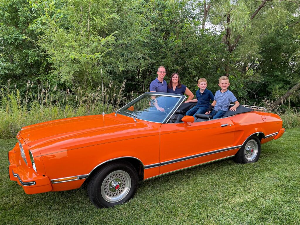 Famille de Robert avec la Mustang II Classic II décapotée, Robert et sa femme à côté, leurs deux fils à l’arrière.
