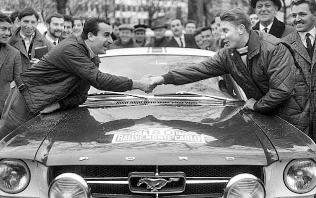 Raphaël Géminiani et Jacques Anquetil se serrent la main au-dessus de la Mustang 180 lors du rallye Monte-Carlo 1965.