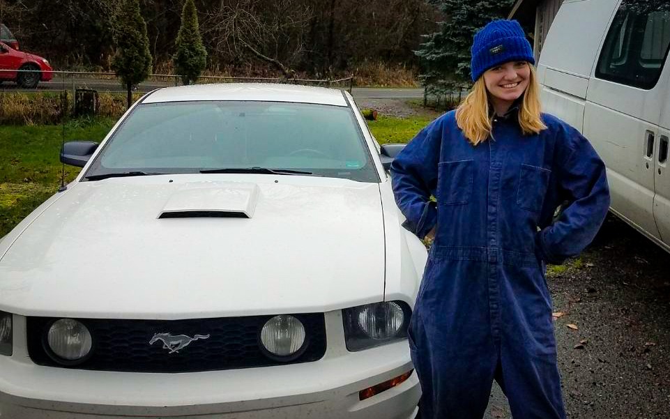 Brittley en combinaison de travail devant sa Mustang GT 2005 blanche Jane