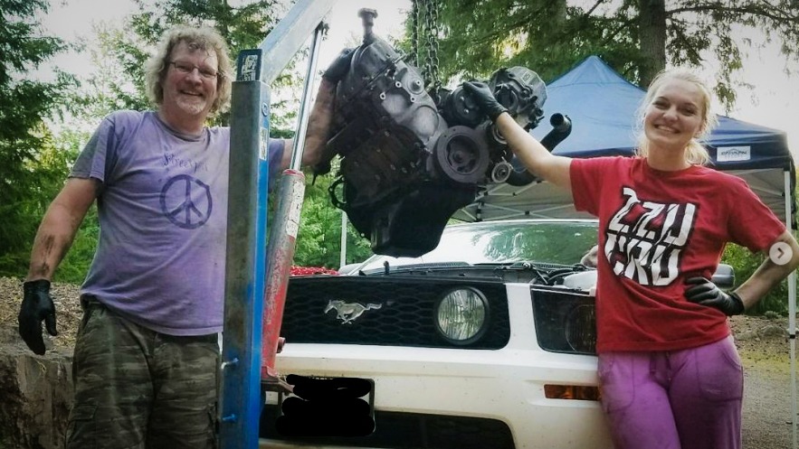 Brittley et son père devant la Mustang GT 2005 blanche avec le moteur déposé sur une chèvre d’atelier